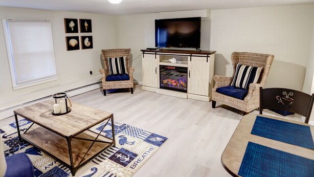 Una sala de estar con televisor, dos sillas de mimbre, una mesa de centro y un mueble con espacio para televisión.