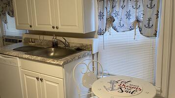 A compact kitchen with white cabinets, a granite countertop, and a small dining area with a table and chairs.