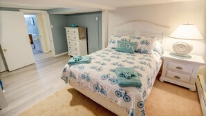 Un dormitorio con cama, mesita de noche, cómoda y una puerta que da a otra habitación.