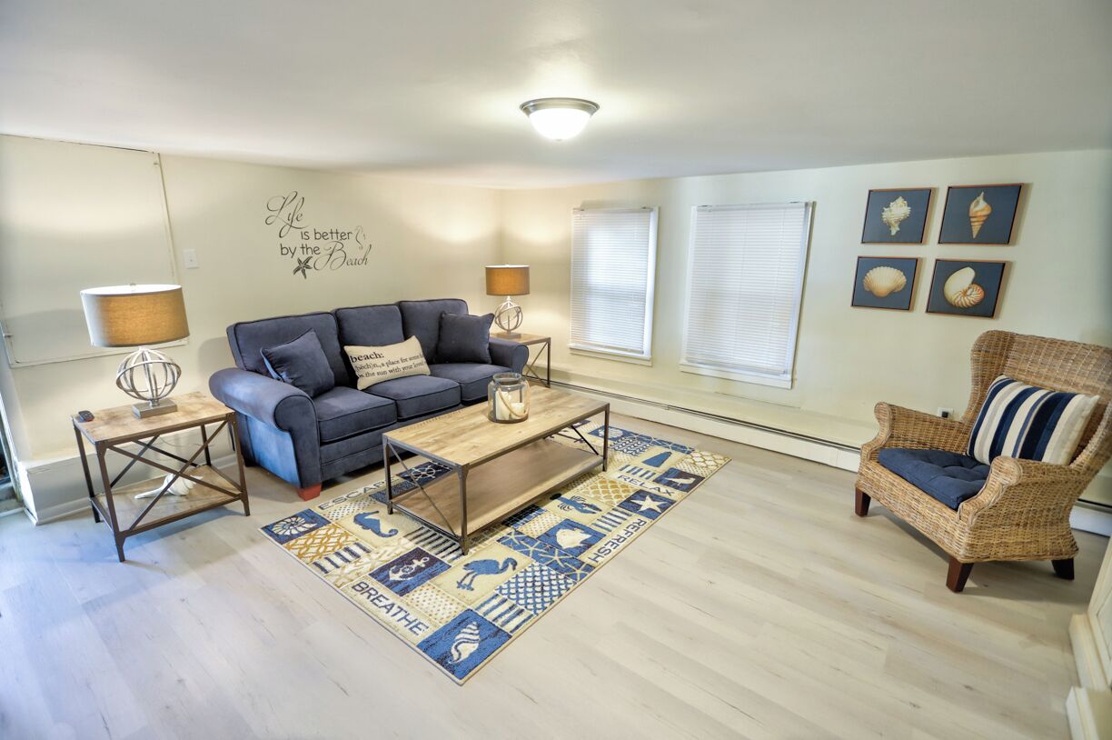 A living room with a grey sofa, a wooden coffee table, a wicker armchair, and a patterned rug.