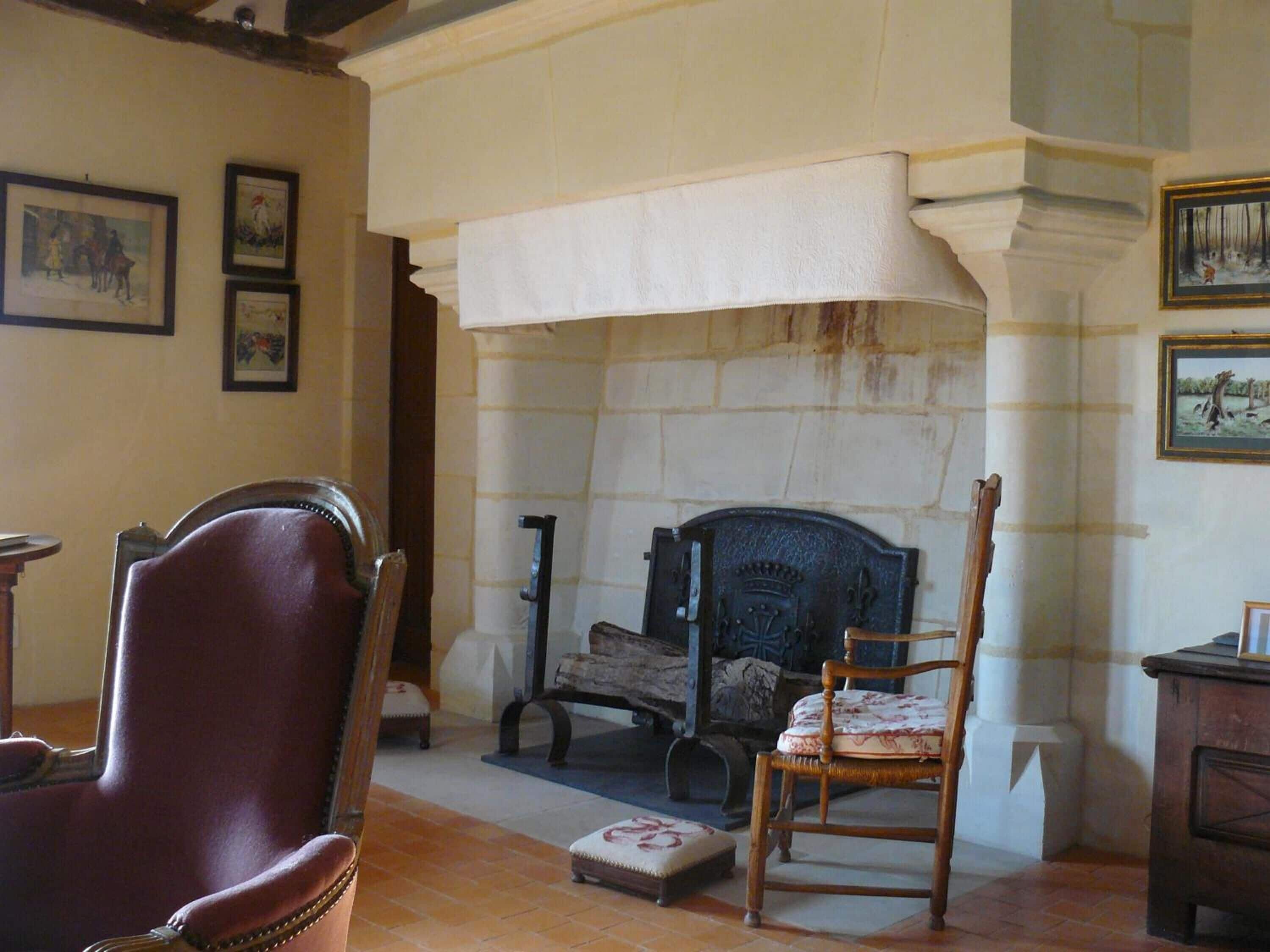 Una habitación con chimenea, dos sillones, una mesita y cuadros en las paredes.