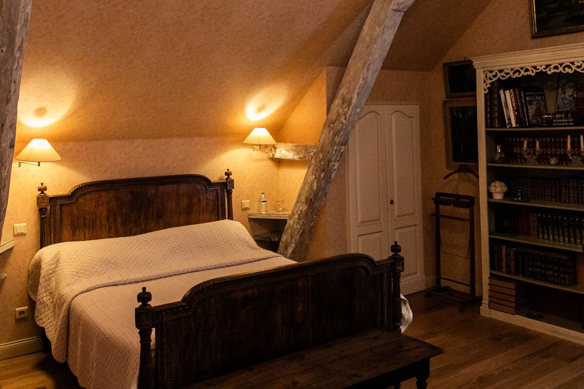 Une chambre à coucher avec un lit en bois, un banc, une bibliothèque et un lustre.
