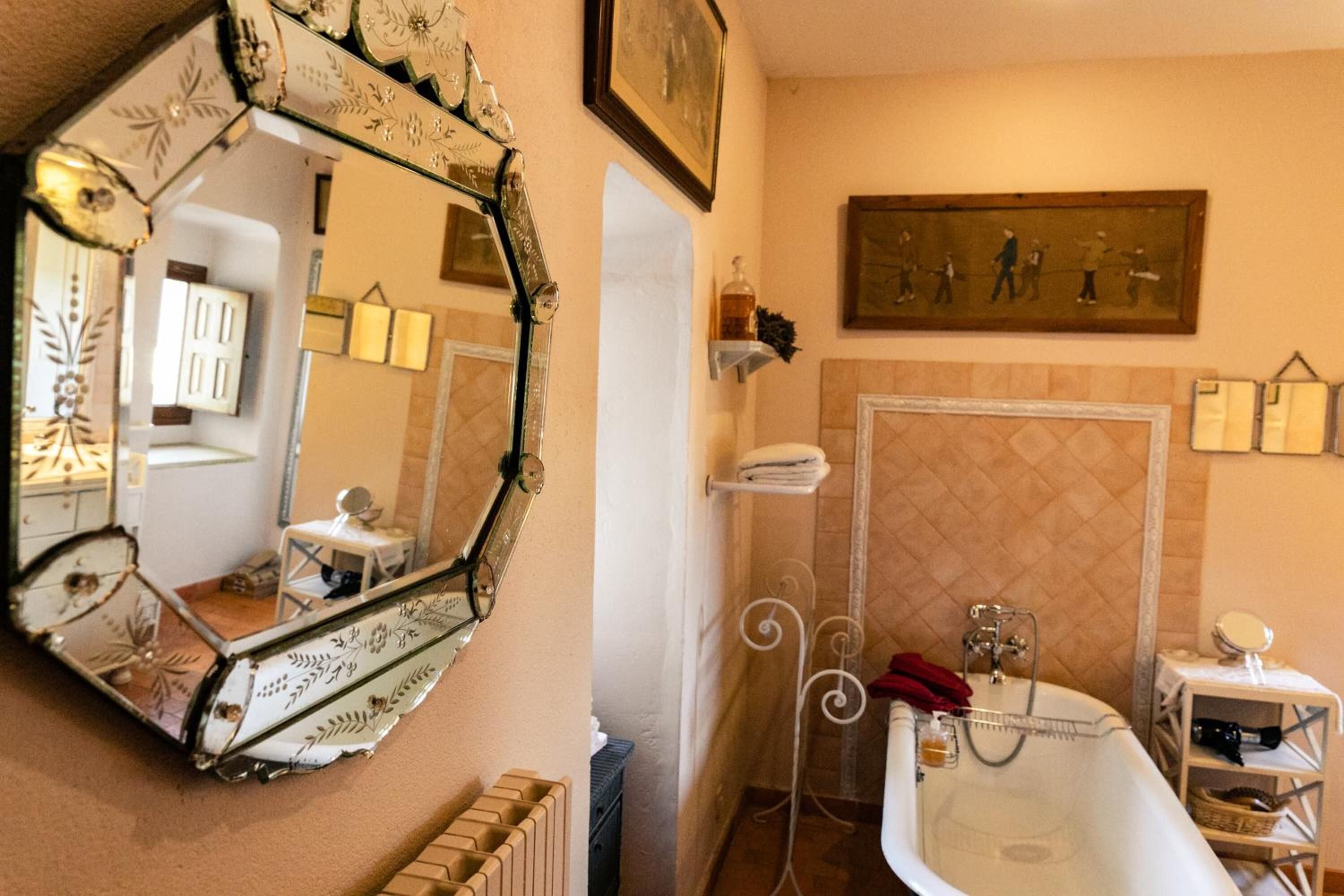 A bathroom with a large mirror, a bathtub, a radiator, and a shelf with toiletries.