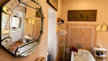 A bathroom with a large mirror, a bathtub, a radiator, and a shelf with toiletries.
