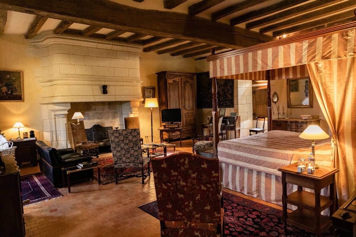 Une chambre traditionnelle dotée d’une cheminée, d’un lit à baldaquin et d’un coin salon avec un canapé et des fauteuils.