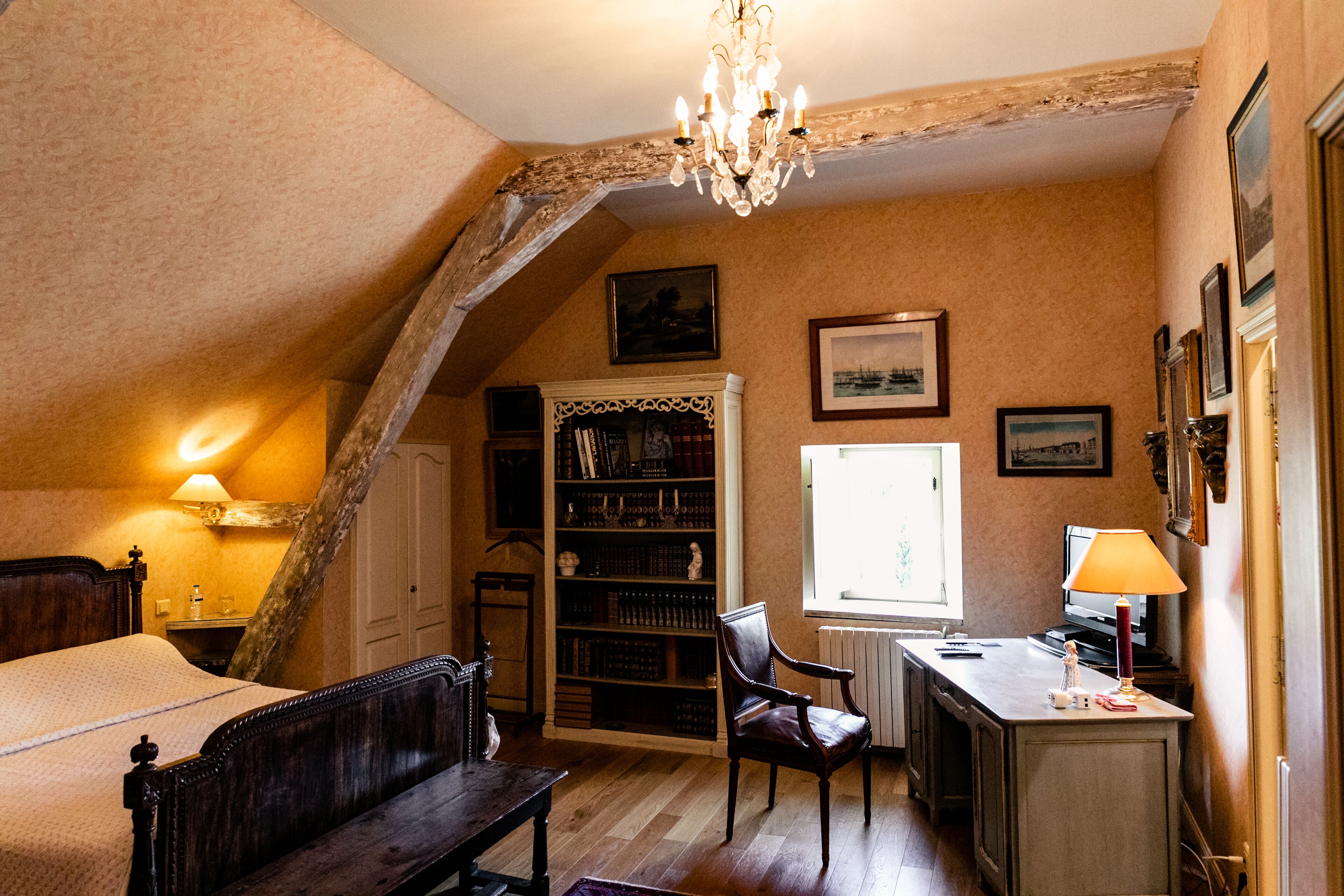 A bedroom with a wooden bed, a desk with a lamp, a bookshelf, and a window with a view.