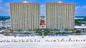 A high-rise hotel with multiple balconies, a central tower, and a beach area with sun loungers. - Calypso 19th Floor Beachfront - Walk to Pier Park - 2 Beachfront Pools (Panama City)