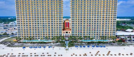 A high-rise hotel with multiple balconies, a central tower, and a beach area with sun loungers.
