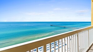 A balcony with a view of the ocean, a pier, and beach umbrellas. - Calypso 19th Floor Beachfront - Walk to Pier Park - 2 Beachfront Pools (Panama City)