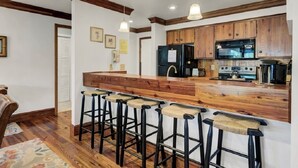 A kitchen with wooden cabinets, a black refrigerator, a stove, and a bar area with stools. - Award-Winning Resort Amenities | Lagoon Villa 3 (Isle of Palms)