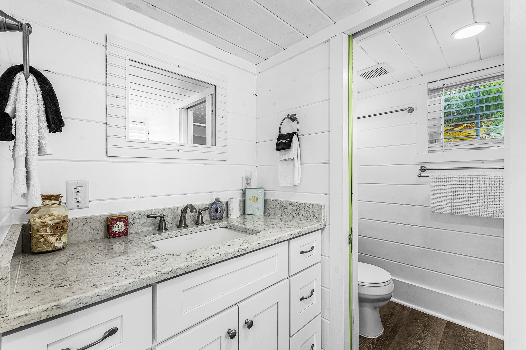Een badkamer met een witte wastafel, een wastafel, een spiegel, een toilet en een douchegedeelte.