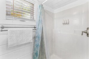 Un baño con ducha, un perchero con una toalla blanca y una ventana con persianas.