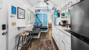 Cocina compacta con zona de estar integrada, refrigerador y ventilador de techo.