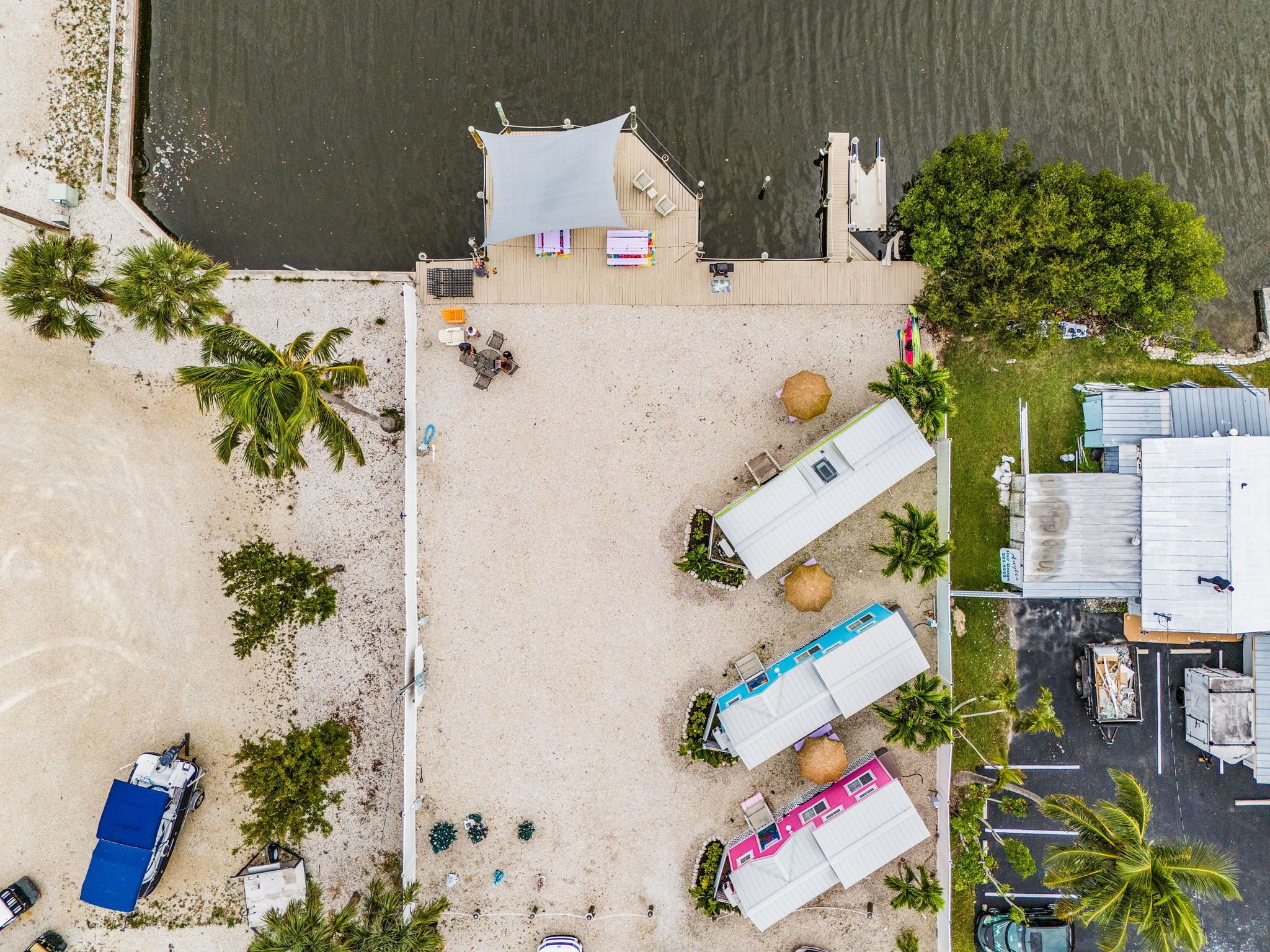 An aerial view of a beachside property with several beach huts, a parking area, and a small building with a sloped roof.