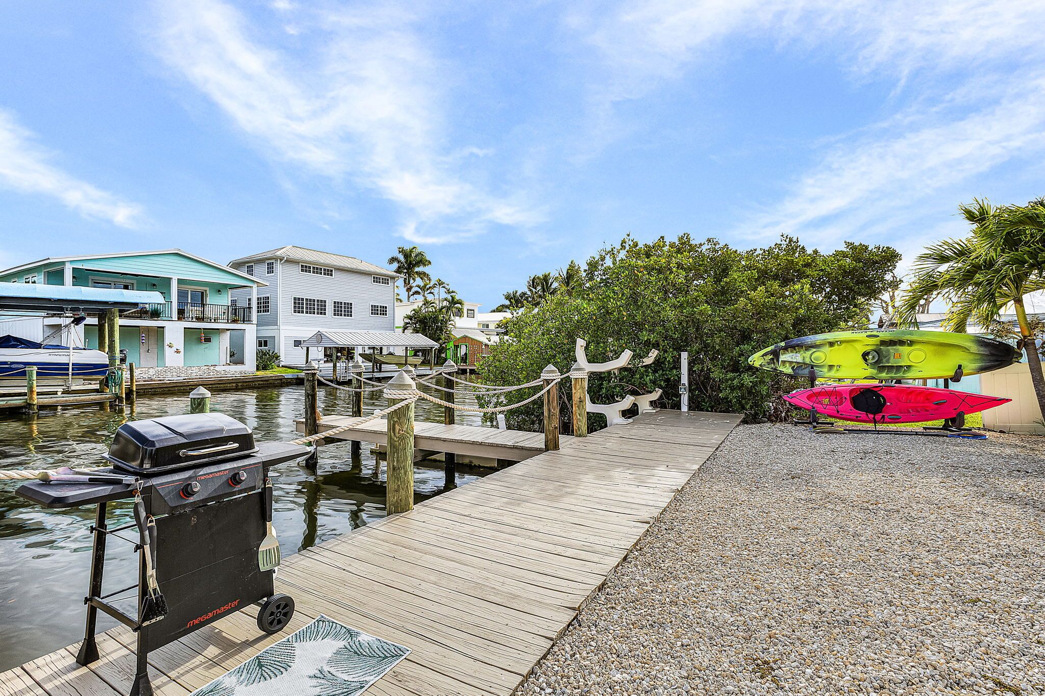 A wooden dock extending into calm water, with a grill cart and kayaks nearby.