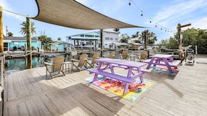 A wooden deck with picnic tables and chairs, a pool, and buildings in the background. - Matlacha Tiny Village (Matlacha)