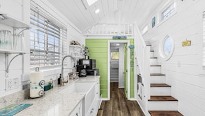 A kitchen with a countertop, sink, and a green door leading to a staircase. - Matlacha Tiny Village (Matlacha)