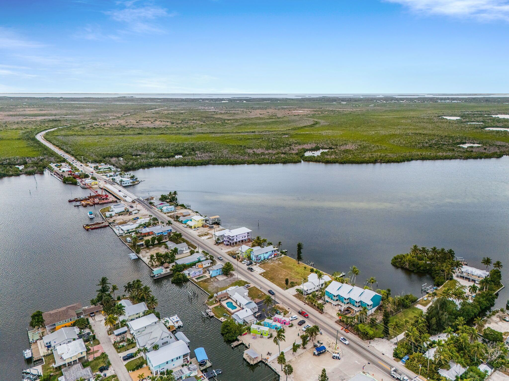 An aerial view of a coastal town with a marina, houses, and a road along the water.