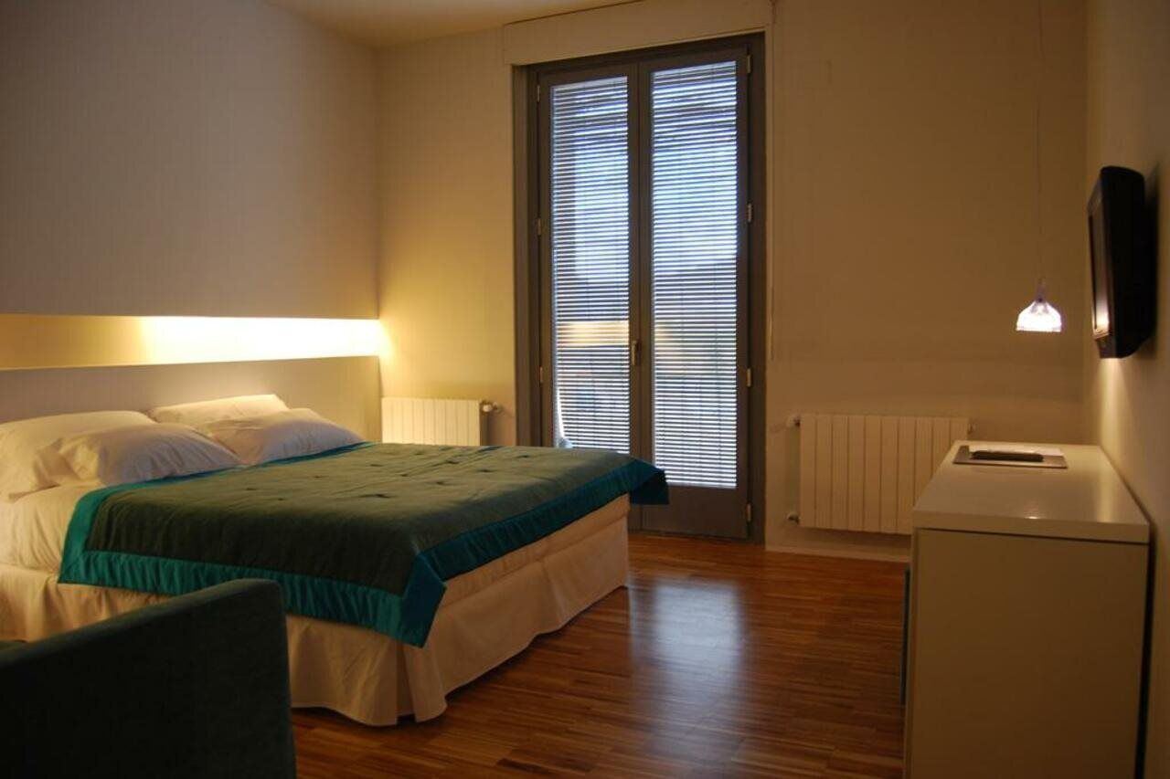 A bedroom with a bed, a desk, and a window with blinds.