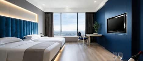 A modern hotel room with two beds, a TV, a dining area, and a view of the city.