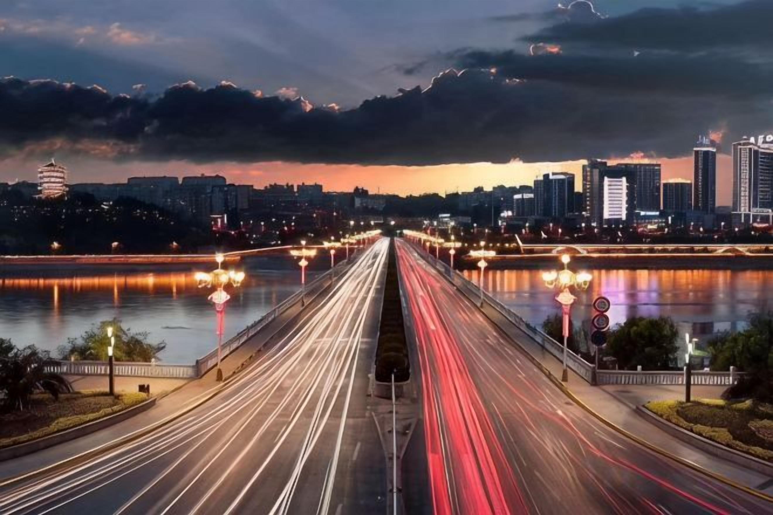A cityscape with a river, a bridge, and a long exposure of moving vehicles.