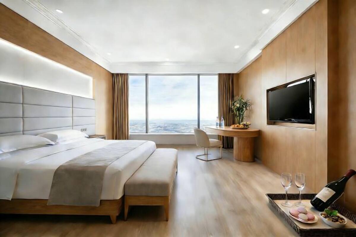A modern hotel room with a large bed, a desk with a chair, a TV, and a city view.