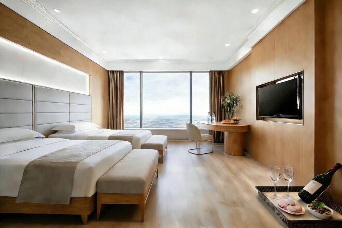 A modern hotel room with two beds, a TV, a dining area, and a view of the ocean.