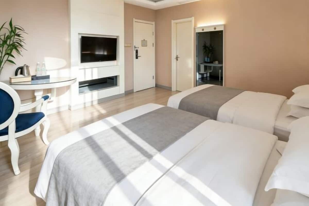 A hotel room with two beds, a TV, a desk, and a chair.