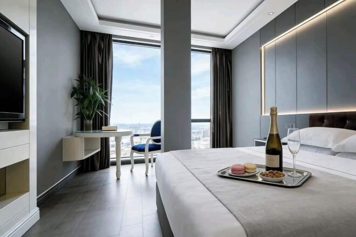 A modern hotel room with a bed, a bedside table, a TV, a window with curtains, and a city view.