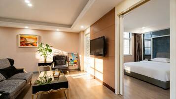 A modern hotel room with a bed, a sofa, a coffee table, a TV, and a painting on the wall.