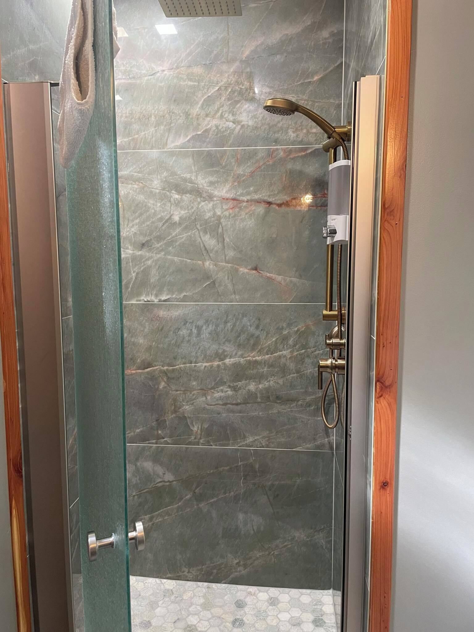 Una ducha moderna con puerta de vidrio, cabezal de ducha de mano y panel de control en la pared.