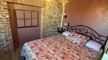 A bedroom with a patterned bedspread, a stone wall, a wooden ceiling, and a hanging light fixture.