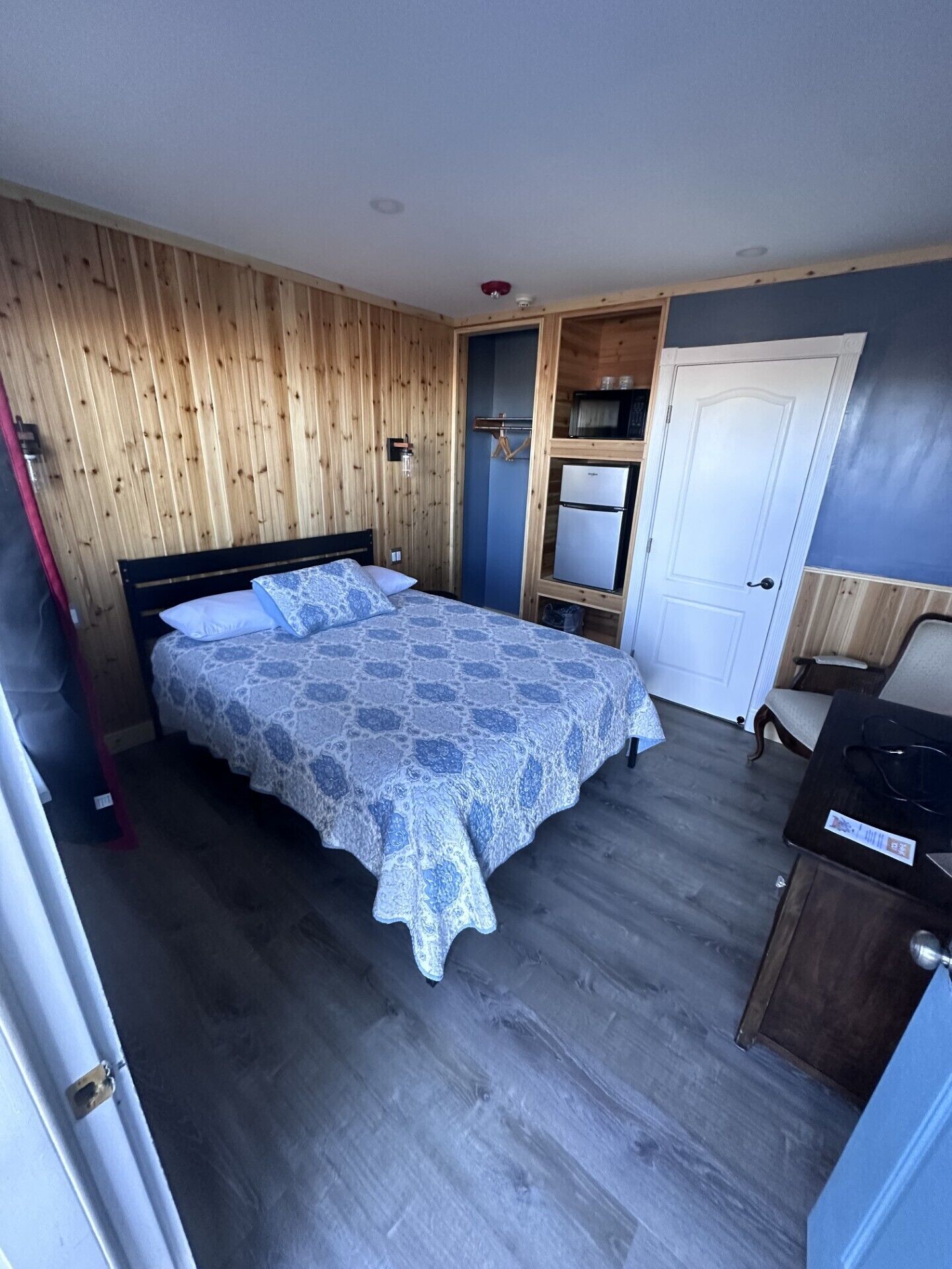 A bedroom with a bed, a wardrobe, a door, and a small kitchenette.
