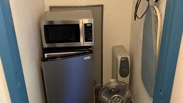 Uma cozinha compacta equipada com micro-ondas, frigorífico e um pequeno ventilador.