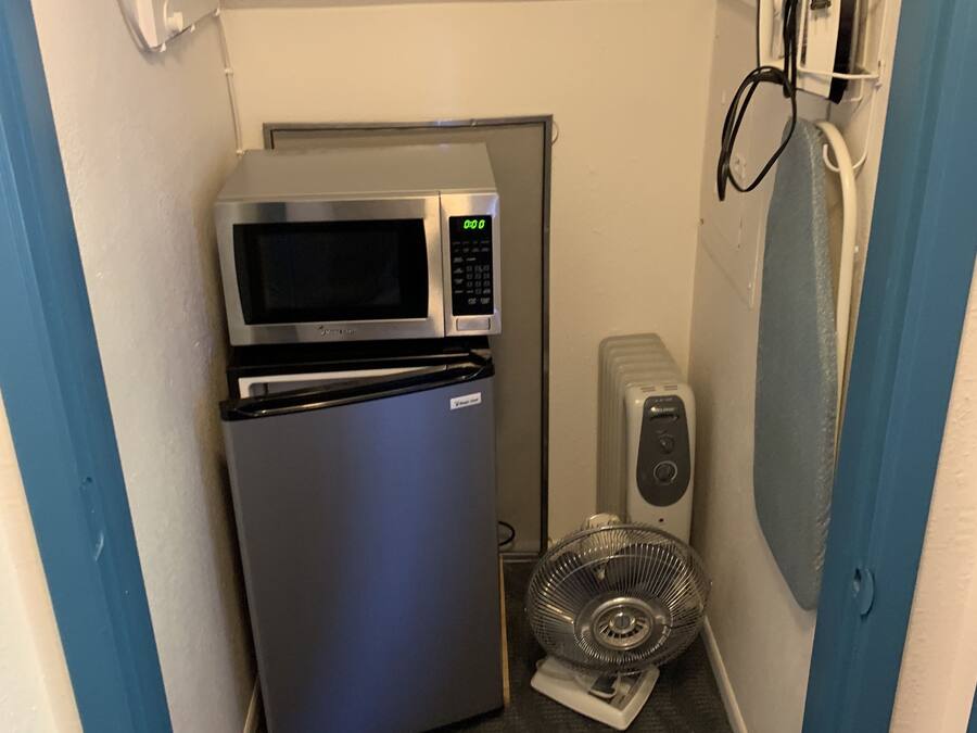 Uma cozinha compacta equipada com micro-ondas, frigorífico e um pequeno ventilador.