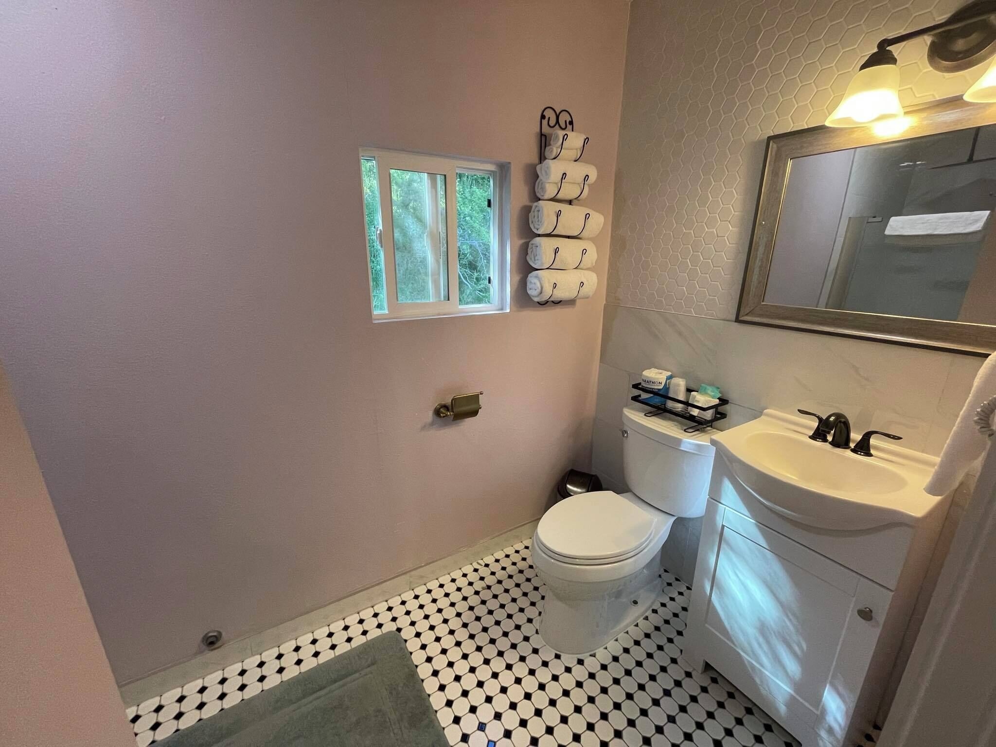 A bathroom with a toilet, sink, and mirror. There is a towel rack with towels and a small window above the toilet.