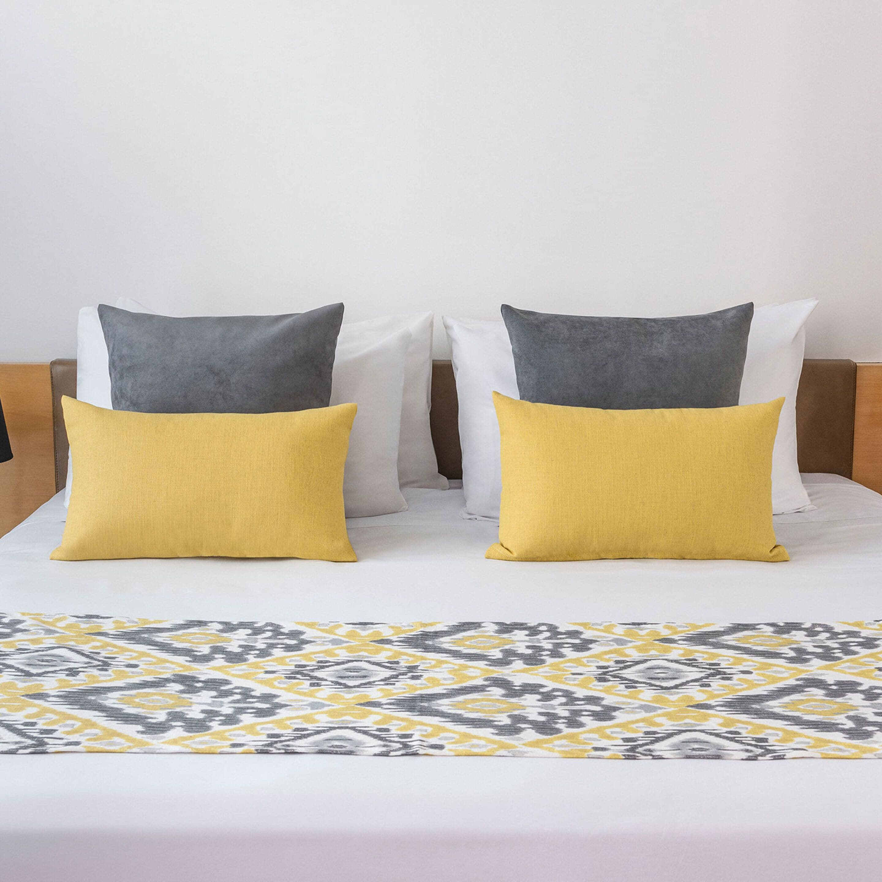 A bed with a patterned bedspread and two pillows, one yellow and one gray.