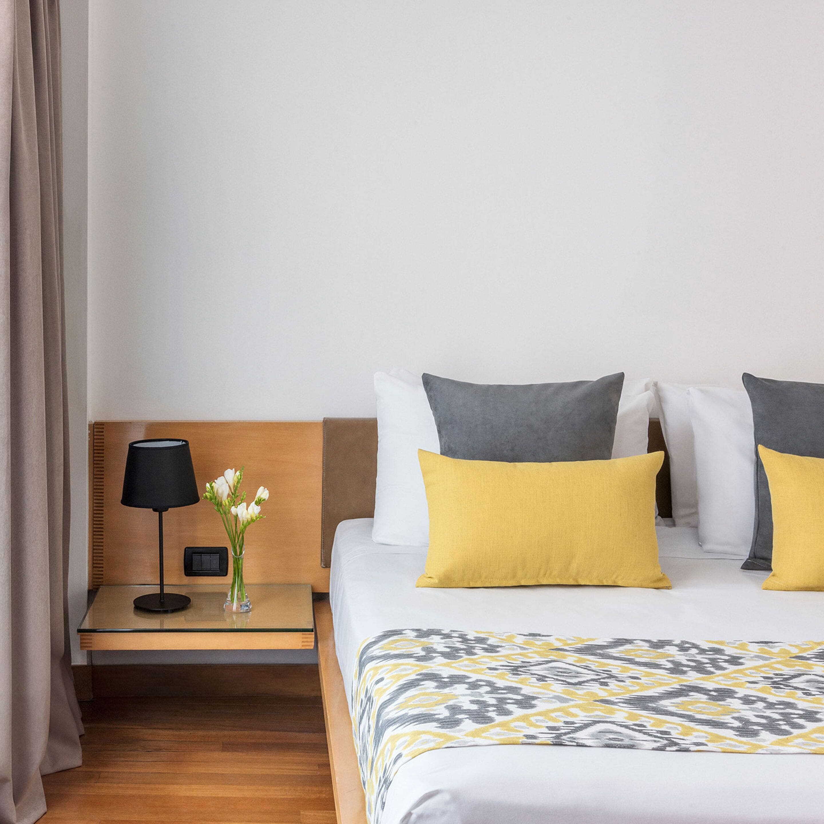 A hotel room with a bed, a nightstand, a lamp, and a vase with flowers.