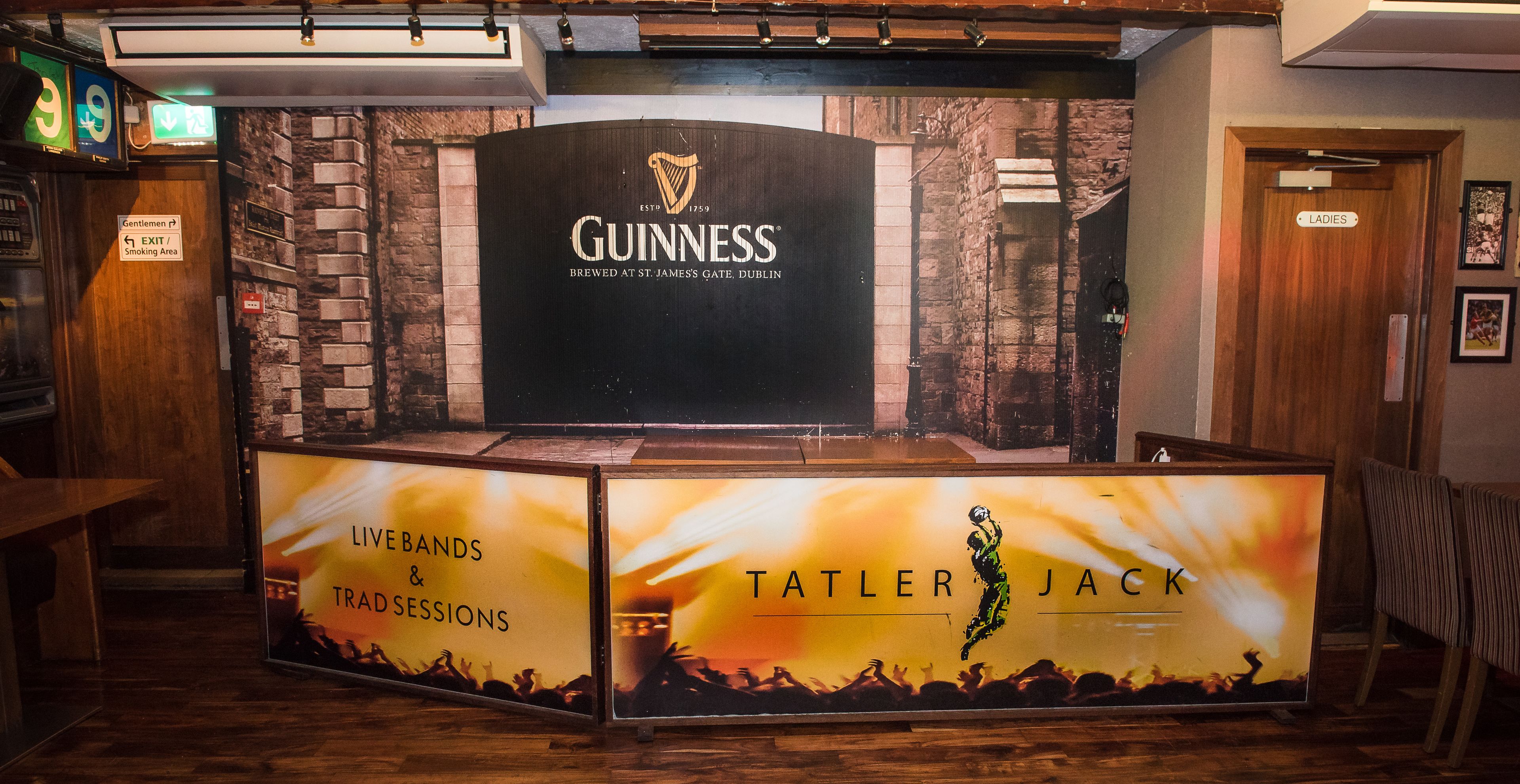 A Guinness branded bar area with a sign for the ladies' room and a sign for the exit and smoking area.