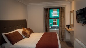 A hotel room with a large bed, a television mounted on the wall, and a window with curtains. - Tatler Jack (Killarney)
