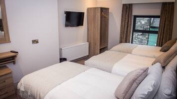 A bedroom with two beds, a TV mounted on the wall, a wardrobe, and a window with curtains.