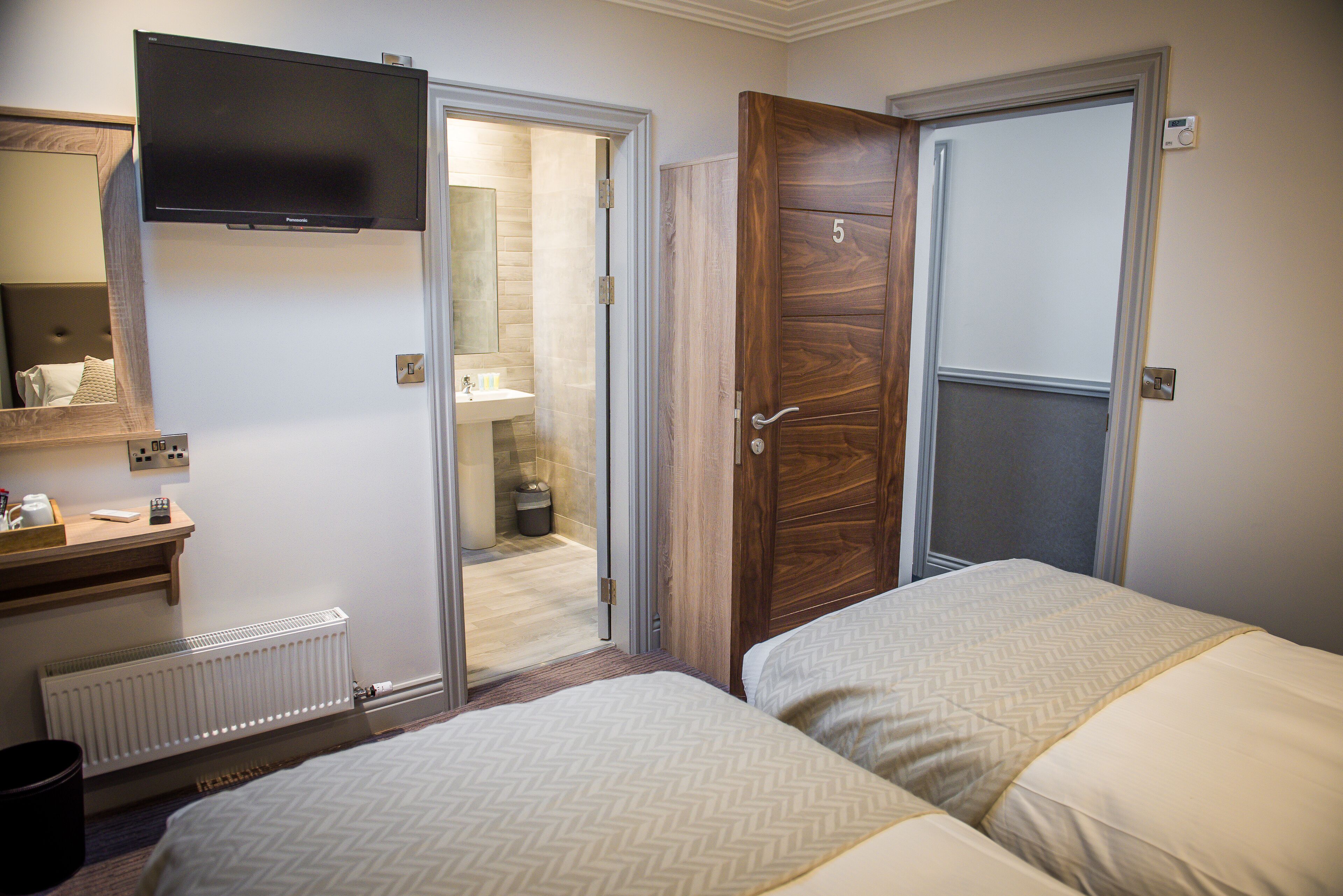 A hotel room with two beds, a TV, a bathroom with a sink, and a wooden door.