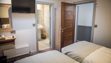 A hotel room with two beds, a TV, a bathroom with a sink, and a wooden door.