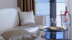 Une chambre d’hôtel avec un canapé blanc, une table en verre sur laquelle se trouvent une bouteille, des verres et une assiette de nourriture.