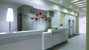 Un comptoir d’accueil moderne avec un plateau blanc, un lampadaire et une œuvre d’art florale fixée au mur.