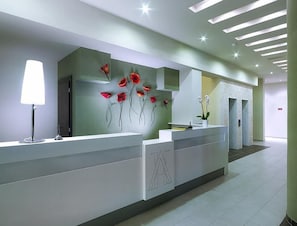 Een moderne receptiebalie met een wit oppervlak, een staande lamp en een bloemkunstwerk aan de muur.