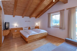 A bedroom with a wooden ceiling, a bed with white bedding, a television on a wooden stand, and a window with curtains.