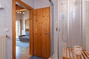 A wooden door leading to a bathroom with a shower and a bench.