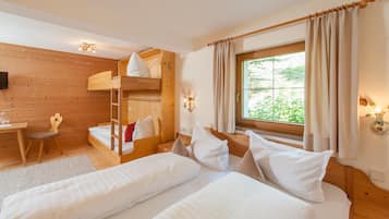 Ein Zimmer mit zwei Betten, darunter einem Schlafsofa, einem Schreibtisch mit Stuhl und einem Fenster mit Vorhängen.
