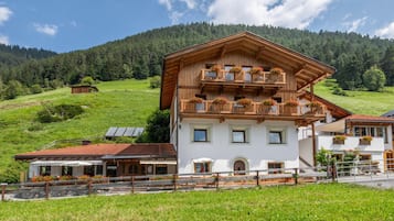 Eine zweistöckige Chalet mit Balkon, umgeben von üppiger grüner Landschaft und einem bewaldeten Berg im Hintergrund.